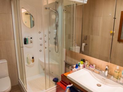 Baño moderno con cabina de ducha acristalada, equipada con múltiples chorros de hidromasaje y un lavabo integrado. Las paredes están revestidas con azulejos beige.