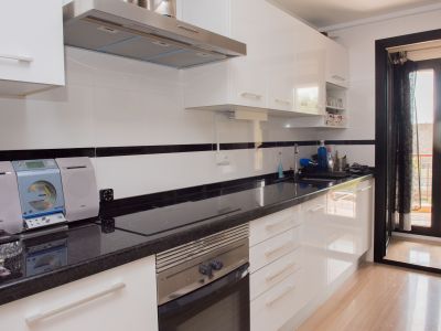 Cocina moderna con armarios blancos brillantes, encimera de granito oscuro, electrodomésticos integrados y acceso a un balcón.