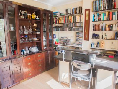 Espacio de estudio con una gran vitrina de madera oscura, estanterías repletas de libros y CDs, y un escritorio moderno con impresora, bañado en luz natural.