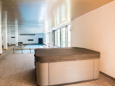 Jacuzzi cubierto en primer plano, con piscina interior climatizada y ventanales que aportan luz natural a esta zona wellness.