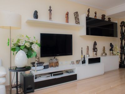 Salón con mueble de TV en blanco y negro, estanterías flotantes exhibiendo esculturas variadas y suelo de gres porcelánico claro. Incluye una lámpara de pie y detalles decorativos.