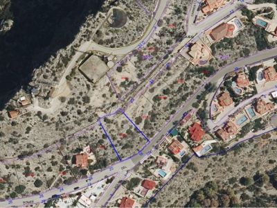 Vista aérea de la parcela urbana, delimitada en azul, ubicada junto a la calle 'ROMER' en la urbanización Monte Pedreguer. Se aprecia el terreno sin desarrollar y propiedades residenciales cercanas.