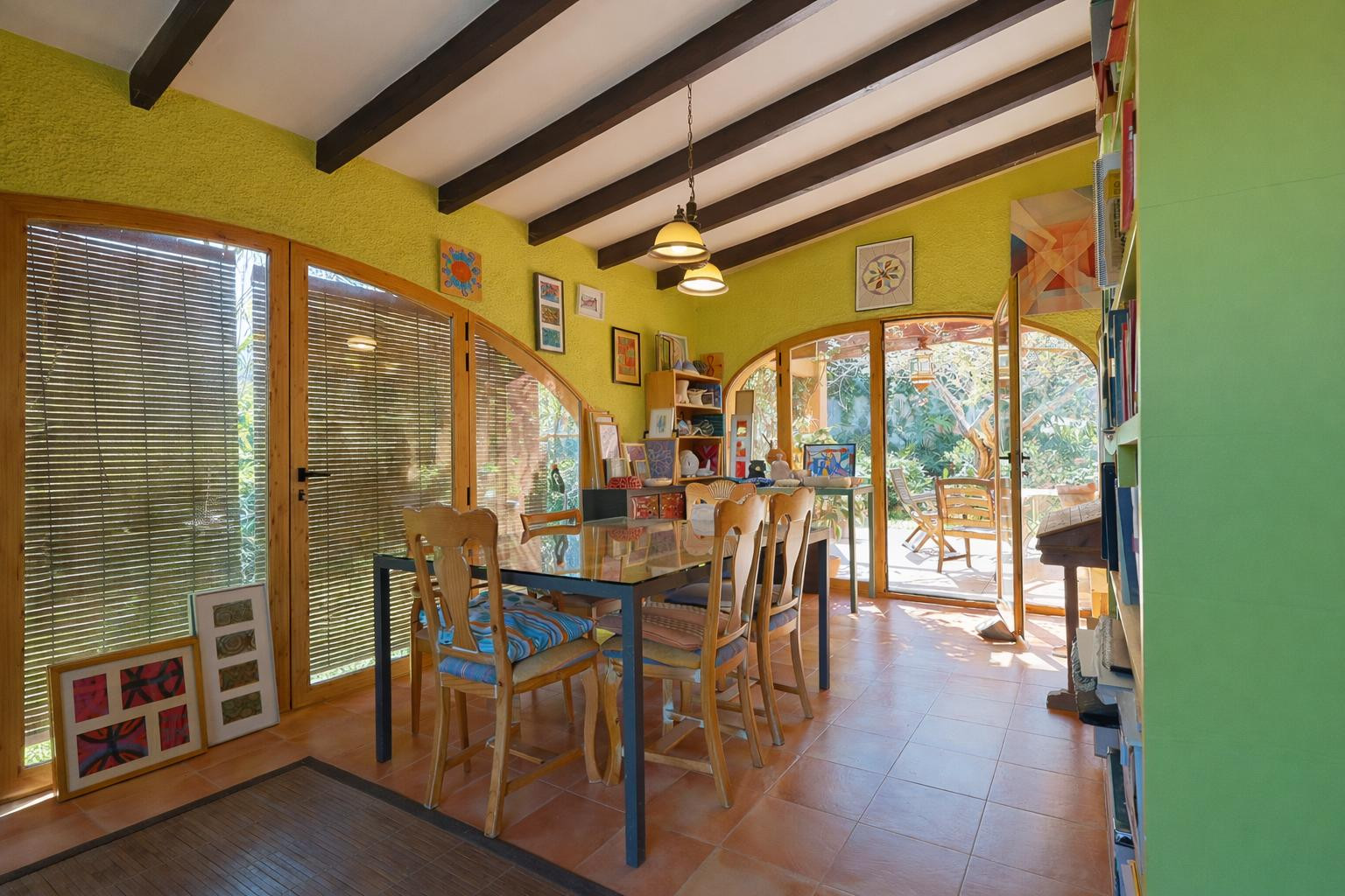 Naya acristalada con vigas de madera, suelos de terracota y grandes ventanales en arco que integran el comedor con el jardín exterior.