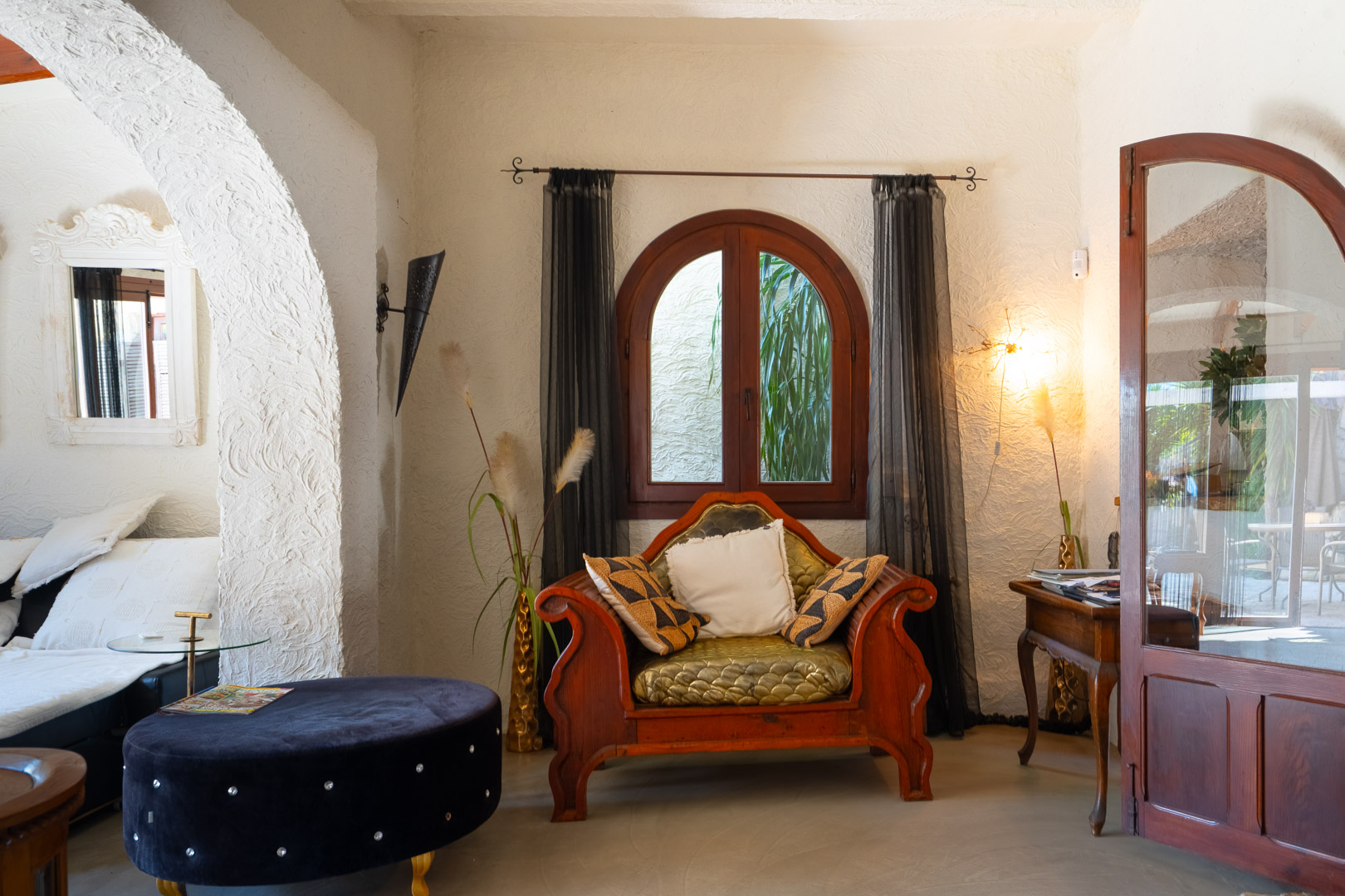 Sala de estar con paredes de yeso texturizado, un sillón de madera tallada y una ventana de arco que aporta luz natural al espacio rústico.