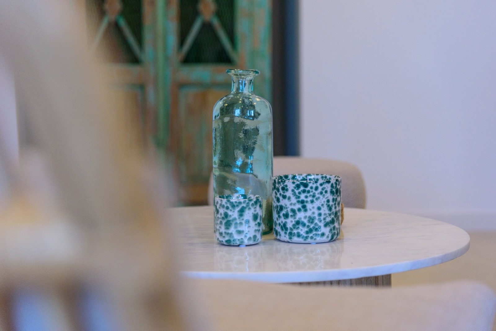 Detalle decorativo sobre mesa de mármol blanco con botella de vidrio turquesa y recipientes cerámicos, resaltando el estilo mediterráneo de la vivienda.
