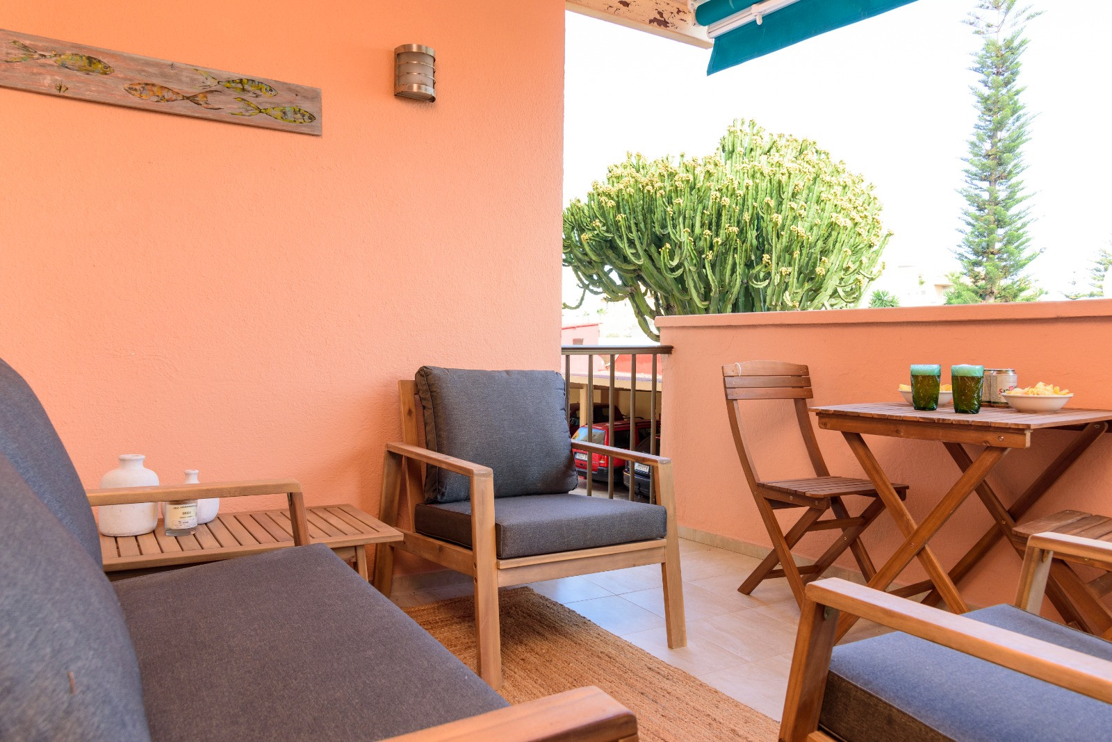 Terraza privada con mobiliario de madera, cojines grises y zona de comedor exterior, rodeada de vegetación local y protegida por un toldo retráctil.