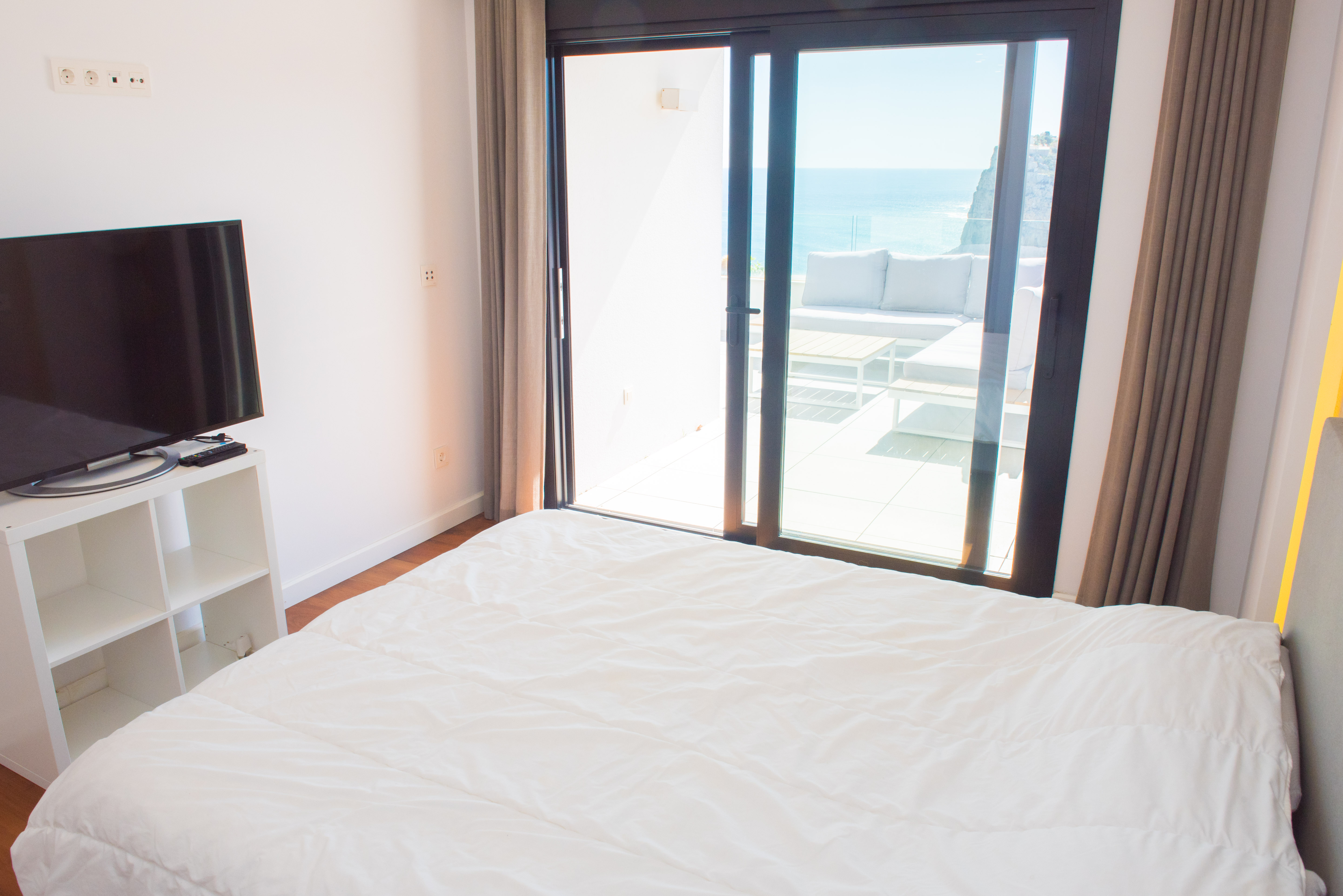 Dormitorio luminoso con acceso directo a una terraza privada equipada con mobiliario exterior y vistas panorámicas al mar Mediterráneo y los acantilados.