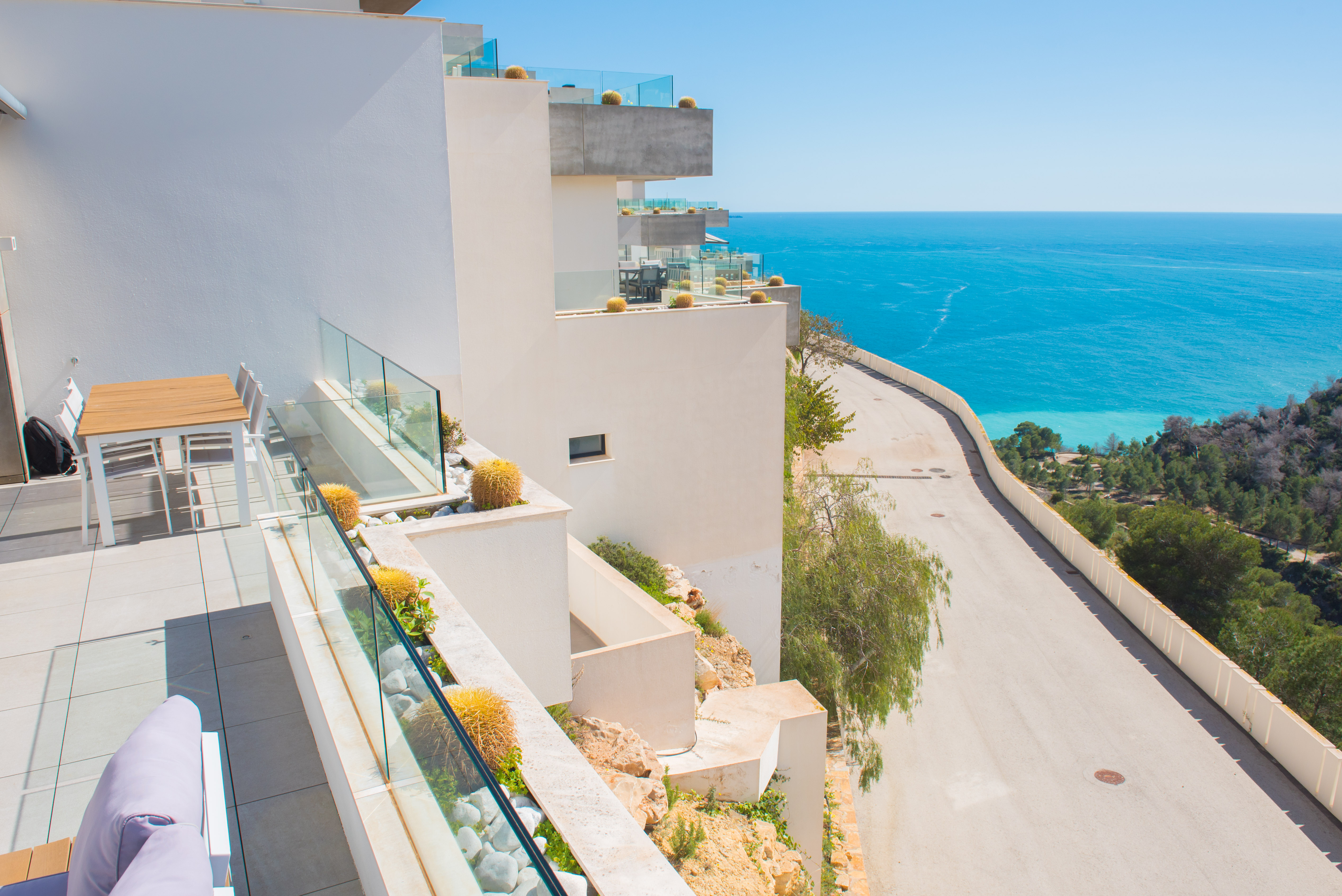 Terraza privada con barandillas de cristal y jardineras integradas con cactus, ofreciendo vistas panorámicas al mar Mediterráneo y la costa de Benitachell.