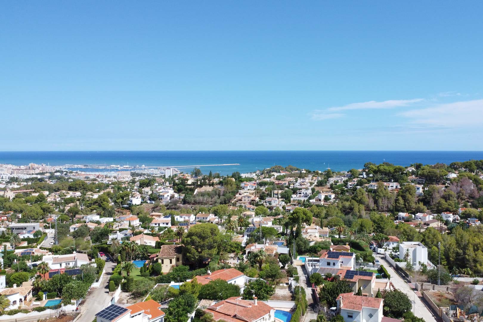 Vista aérea panorámica de la zona residencial de Dénia con vistas al mar Mediterráneo, el puerto y un entorno consolidado de viviendas unifamiliares con piscinas.