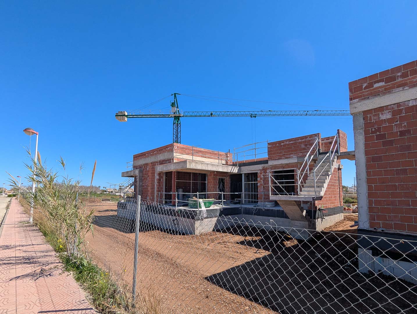 Estado actual de la construcción mostrando la estructura de ladrillo cerámico, forjados de hormigón y escalera exterior en una parcela llana bajo un cielo despejado.