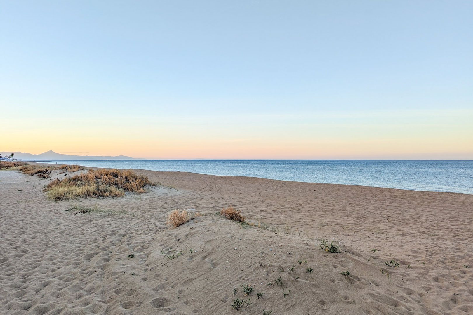 Playa de arena fina con dunas naturales y vegetación autóctona situada a menos de dos kilómetros de la vivienda. Vista del mar Mediterráneo y montañas al fondo al atardecer.