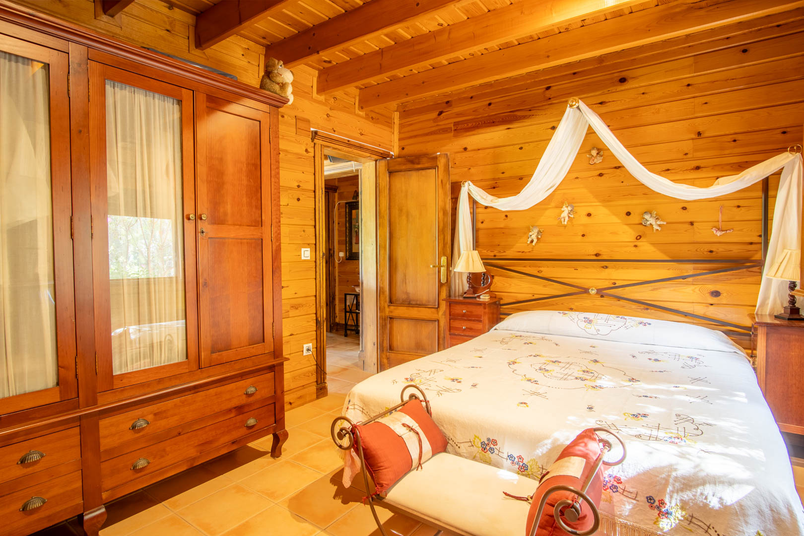 Dormitorio rústico con paredes y techos de pino finlandés, armario de madera maciza y una cama doble con dosel decorativo y cabecero de forja.