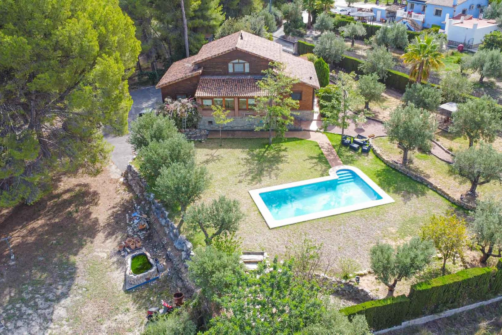 Vista aérea de la villa de madera de pino finlandés con piscina privada, rodeada de jardines mediterráneos con olivos y pinos en una amplia parcela en Orba.
