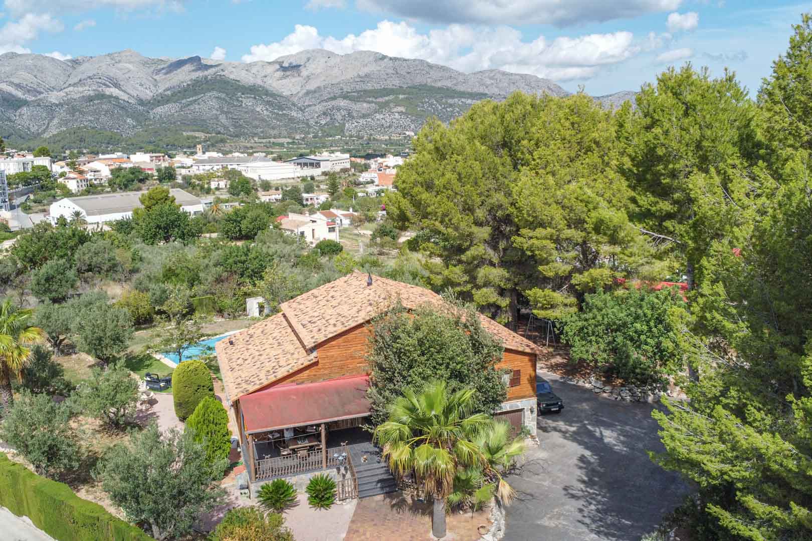 Vista aérea de la villa de madera de pino finlandés rodeada de vegetación mediterránea, con vistas panorámicas a las montañas y al pueblo de Orba.