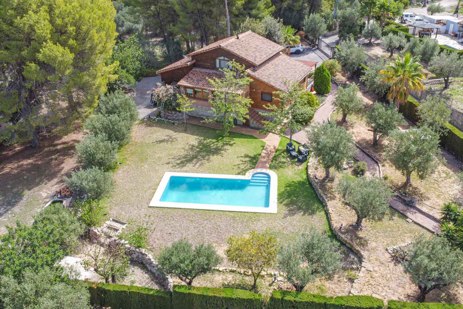 Vista aérea de la villa de pino finlandés y piedra, destacando la piscina privada rodeada de olivos y jardines mediterráneos en una amplia parcela en Orba.