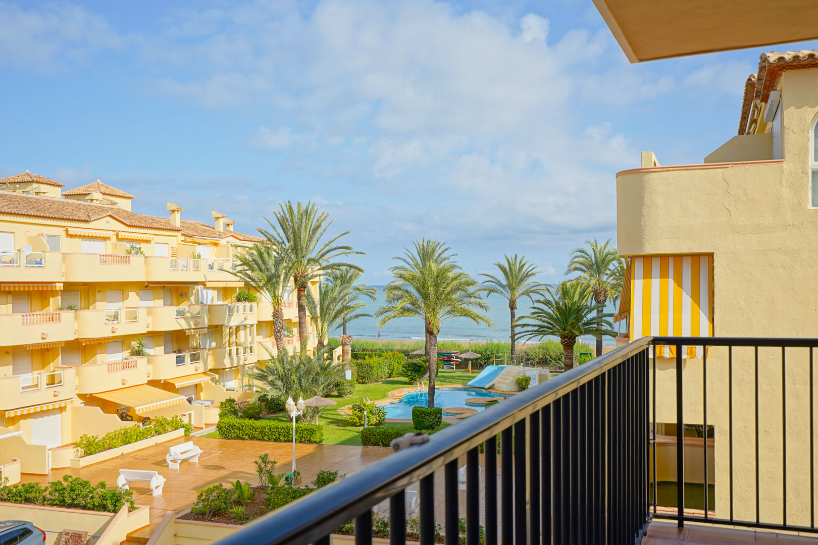 Vistas desde un balcón privado hacia un complejo residencial con piscina, zonas ajardinadas y panorámica directa al mar Mediterráneo.