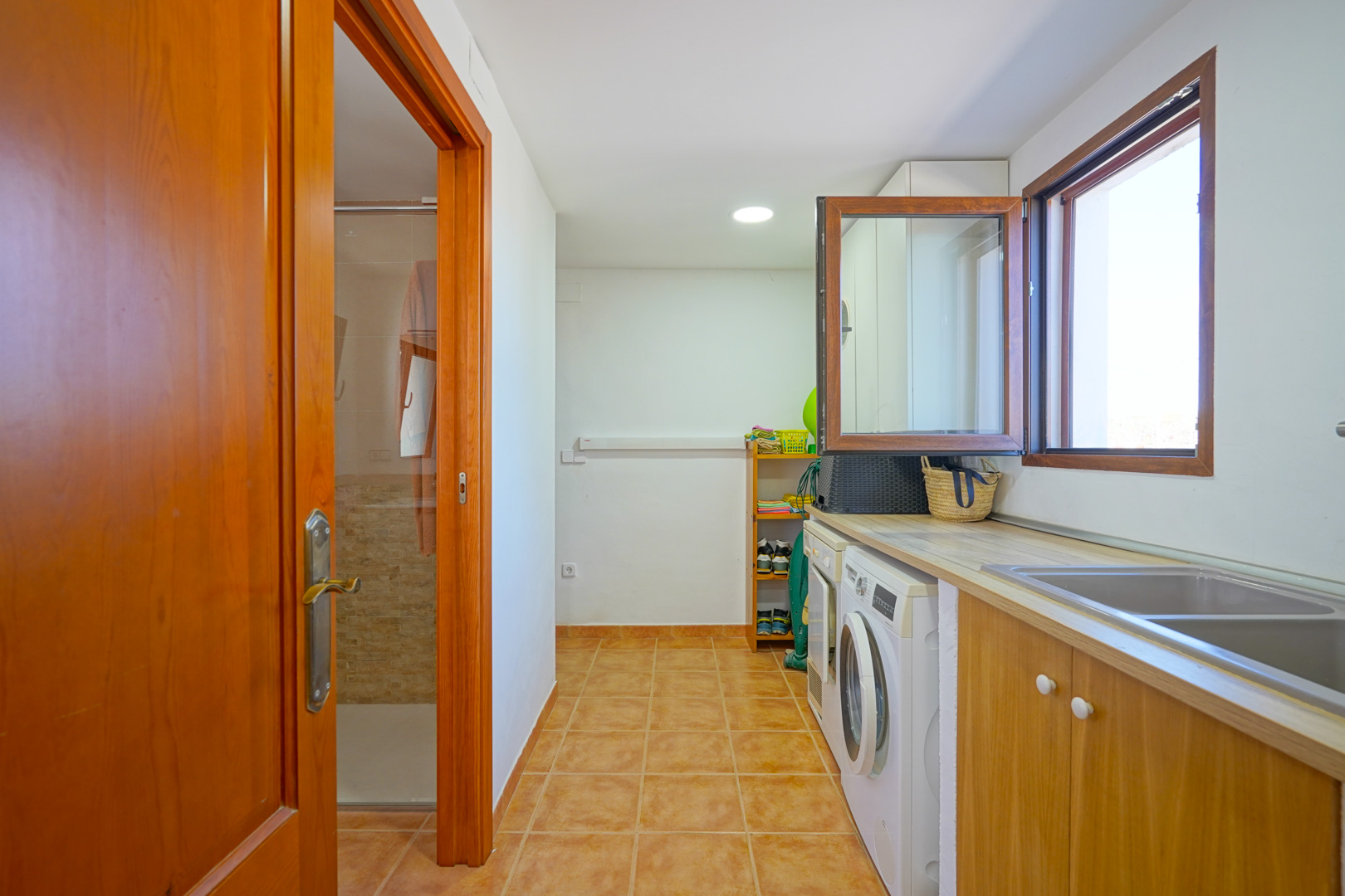 Amplio lavadero equipado con lavadora, secadora y fregadero doble bajo encimera de madera, con acceso directo a un baño con ducha.