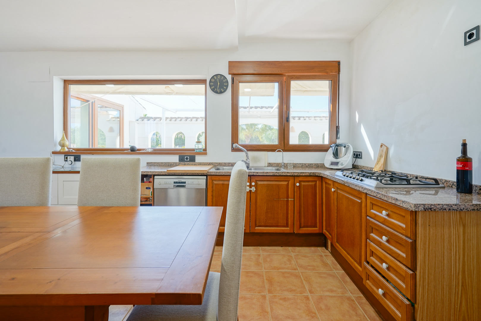 Cocina rústica con encimera de granito, armarios de madera y zona de comedor. Amplios ventanales ofrecen vistas al patio exterior y aportan abundante luz natural.