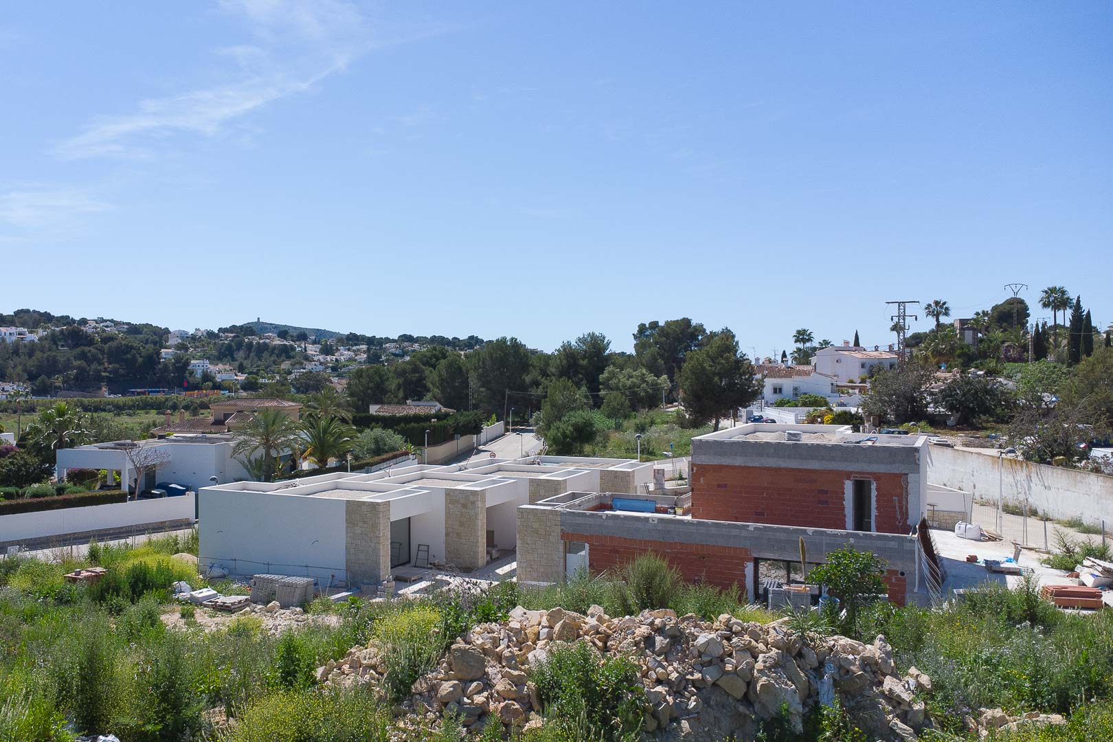 Vista exterior de la propiedad en fase de construcción, destacando los muros de piedra natural y la estructura moderna integrada en el entorno de Moraira.