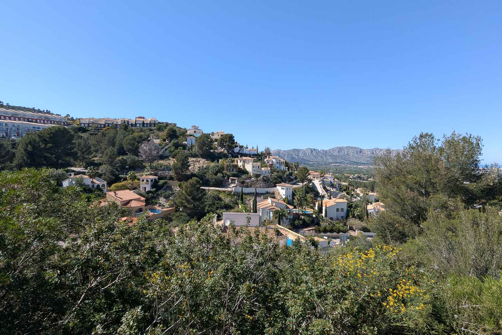 Vista panorámica de la urbanización con casas de tejas rojas y vegetación exuberante bajo un cielo azul.
