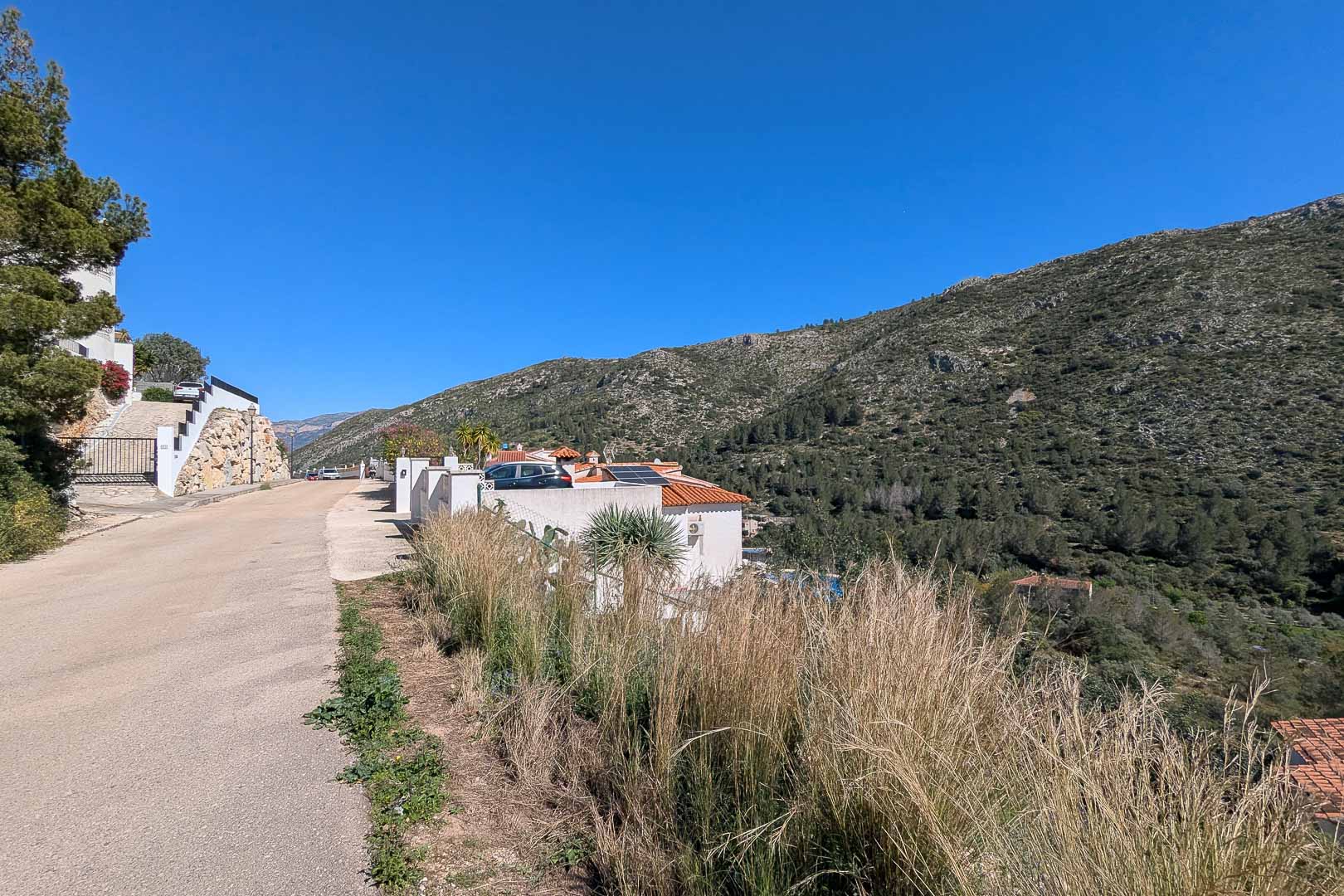 Vista exterior de la villa desde el camino de acceso, resaltando los paneles solares en el tejado y el entorno natural de las montañas de Pedreguer.