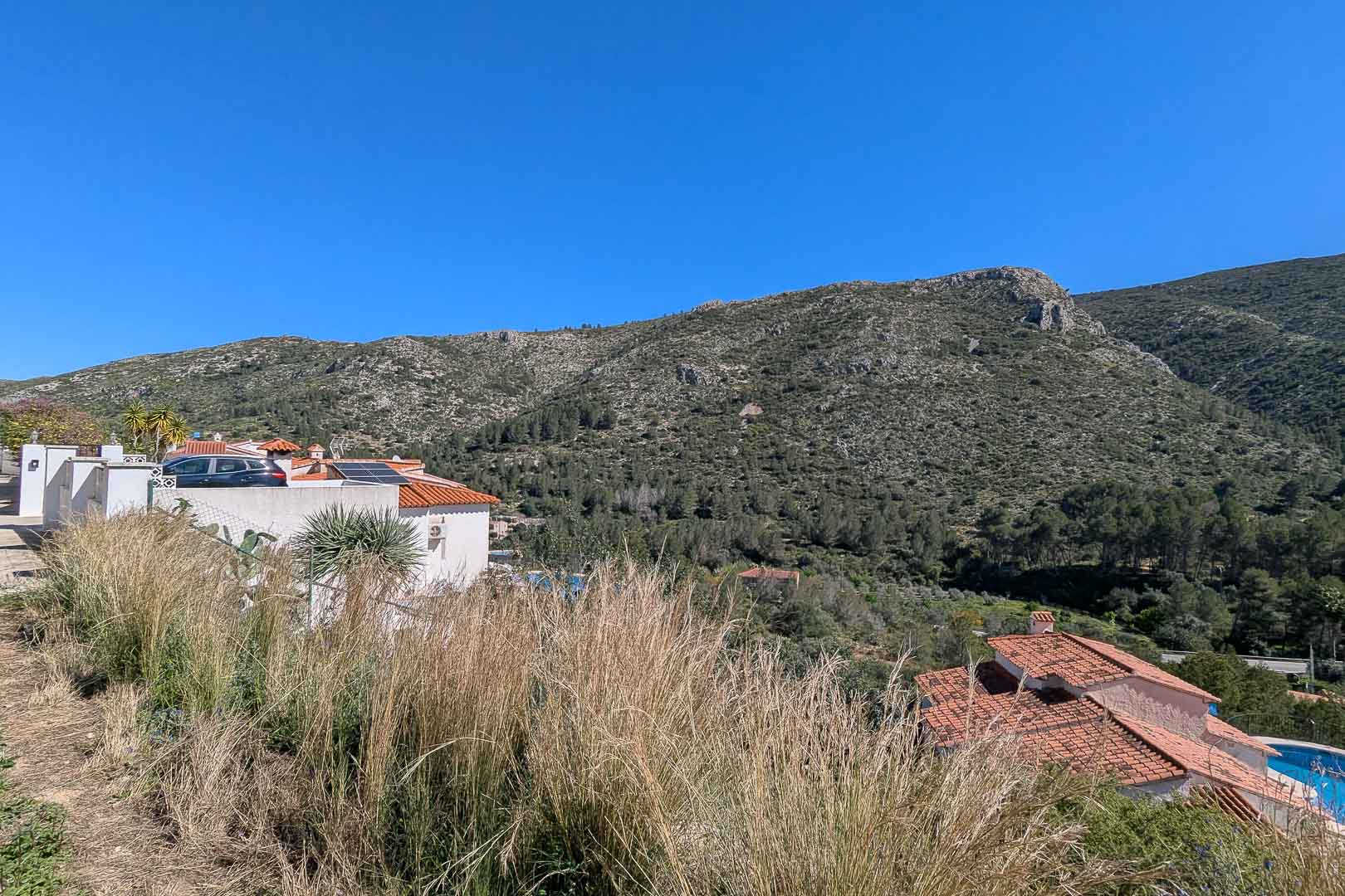 Vistas panorámicas a las montañas y al valle desde la parcela, destacando el entorno natural y las viviendas vecinas de estilo mediterráneo.