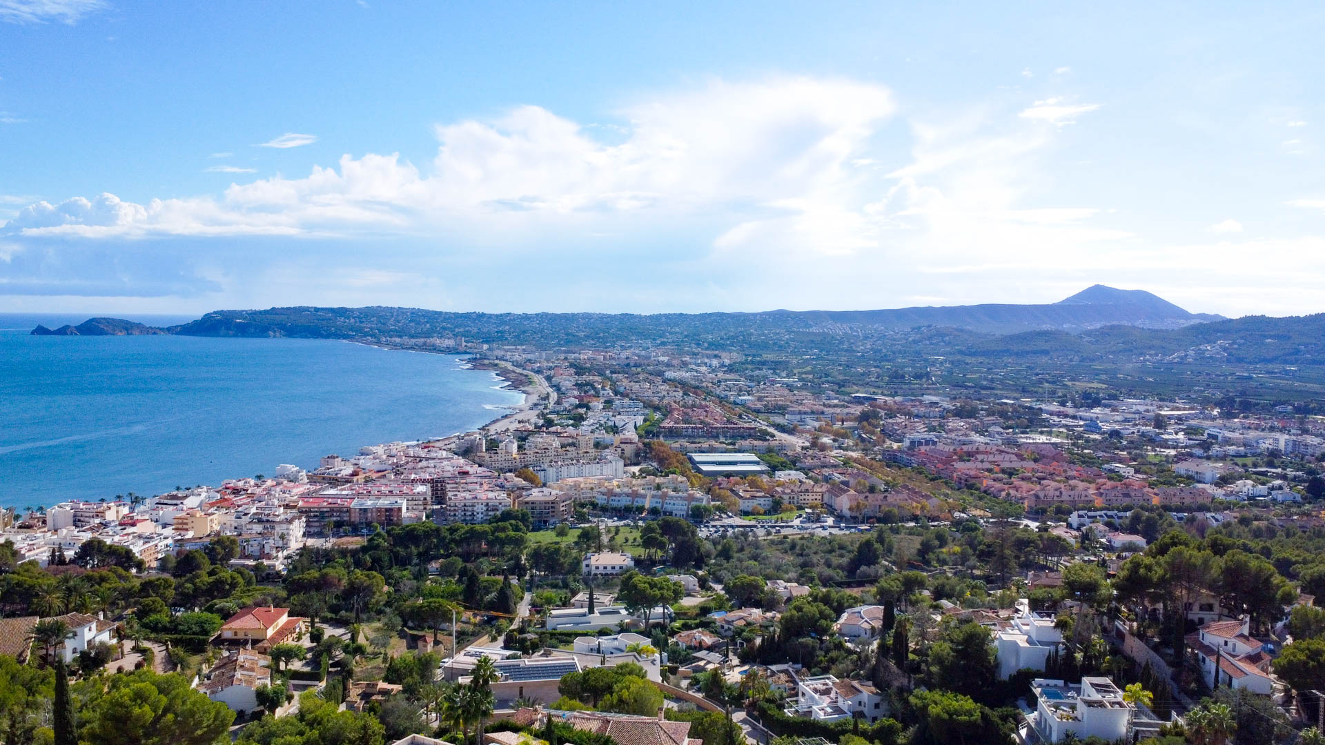 Vista aérea panorámica de la bahía de Jávea y el puerto desde La Corona, mostrando la costa mediterránea y el perfil del Montgó al fondo.