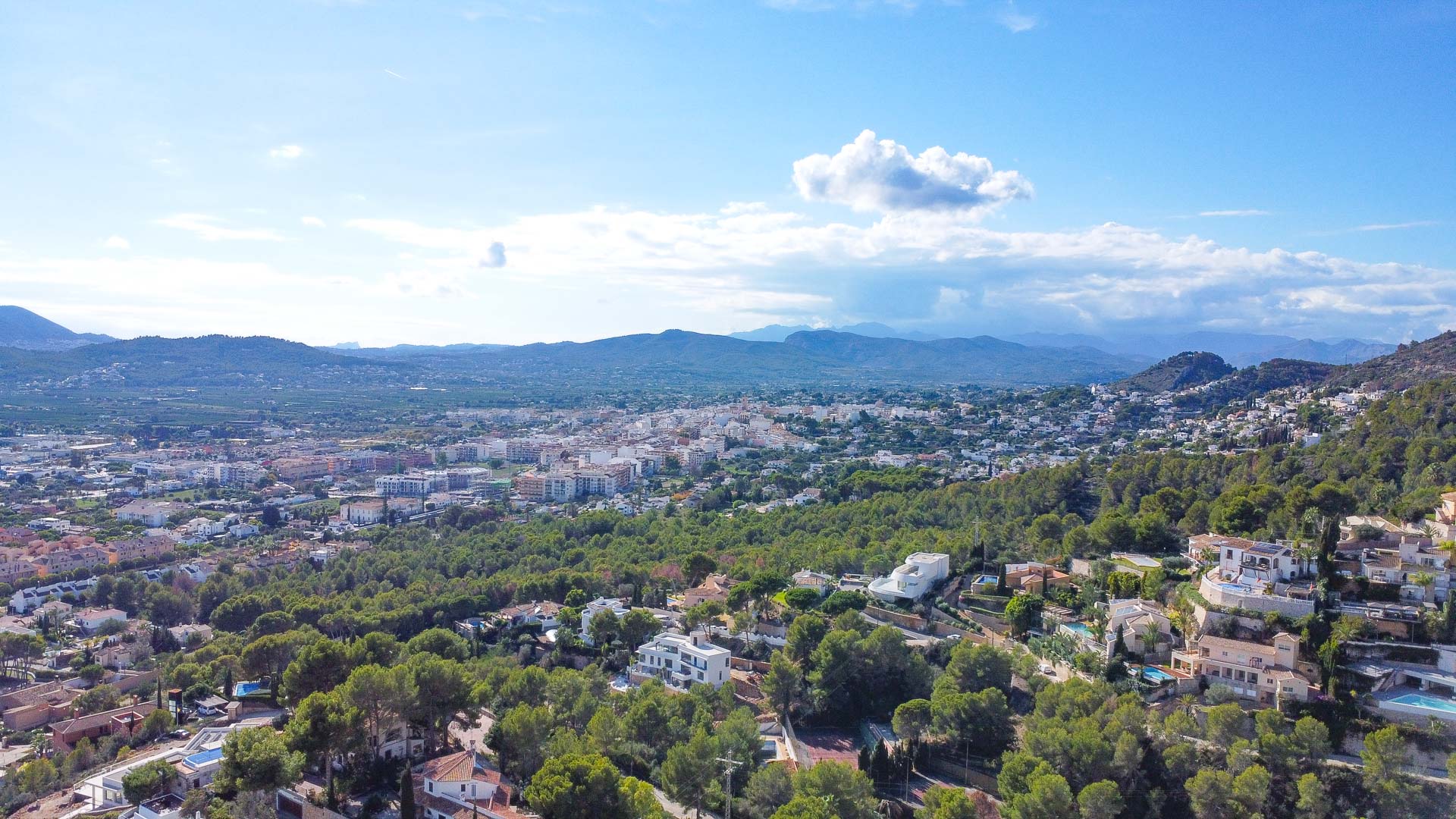 Vista aérea panorámica desde la urbanización La Corona, mostrando el entorno natural de pinos y la extensión urbana de Jávea hacia las montañas del horizonte.