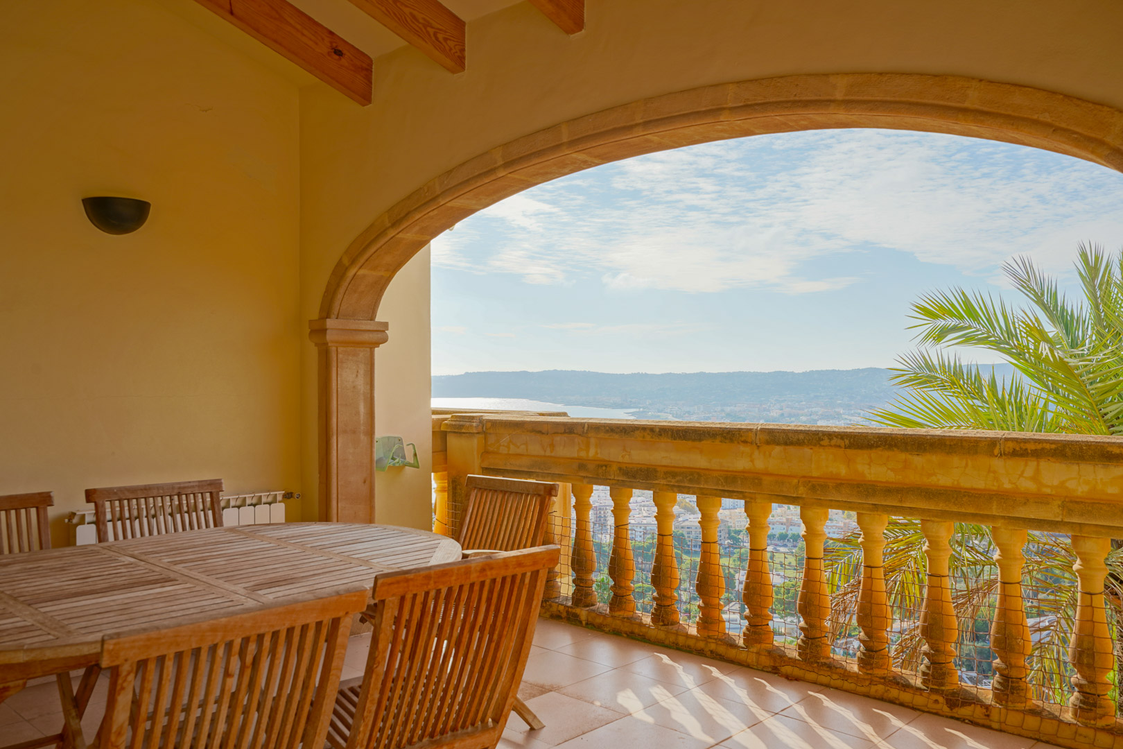 Terraza cubierta con vigas de madera y arco de piedra tosca, equipada con mobiliario de madera y vistas panorámicas a la bahía de Jávea y las montañas.