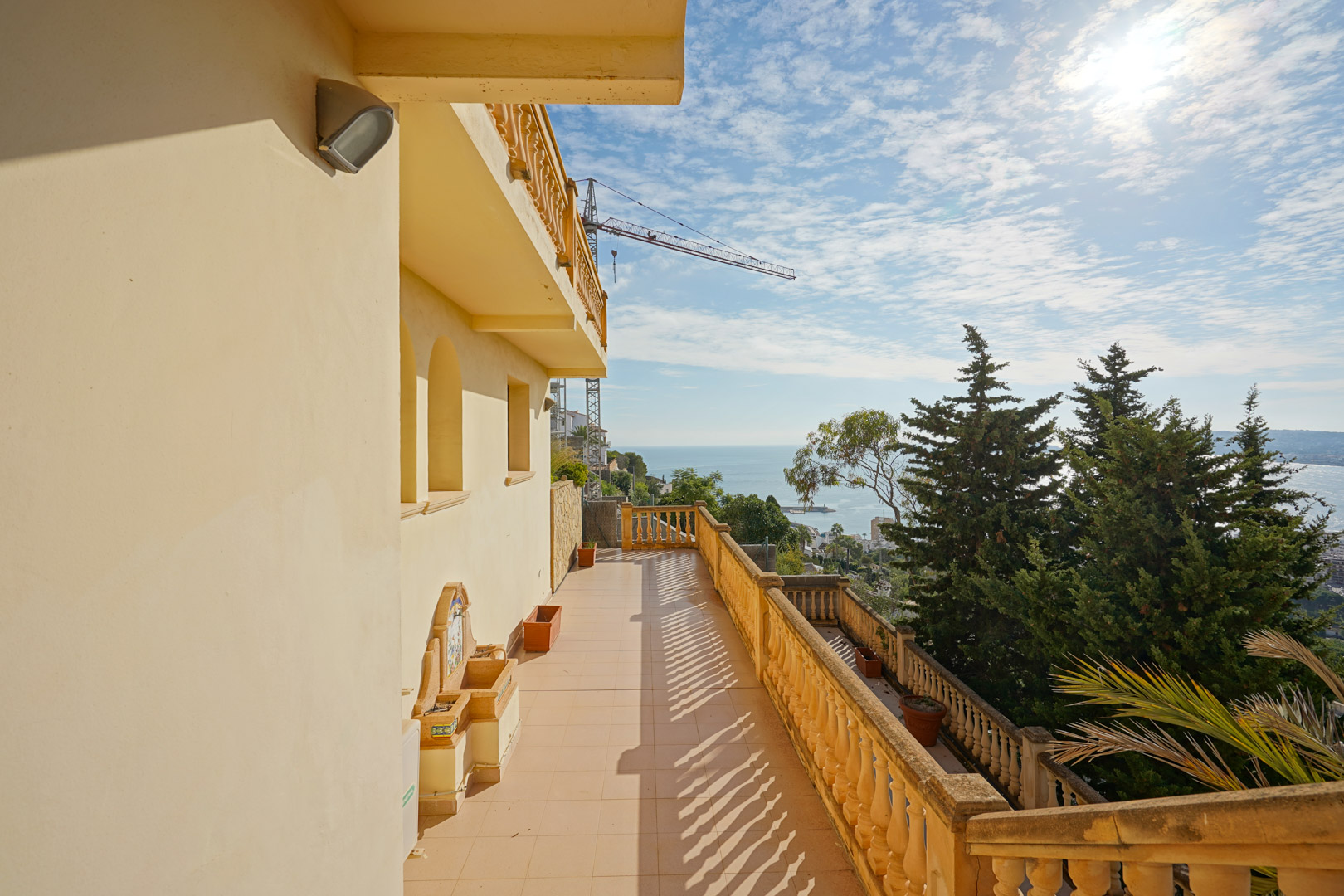Terraza longitudinal con balaustrada tradicional y vistas panorámicas al mar Mediterráneo, incluyendo una fuente decorativa de piedra y suelos cerámicos.