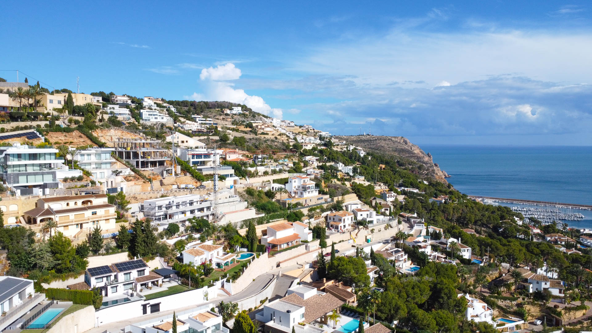 Vista aérea de la urbanización La Corona en Jávea, destacando la disposición escalonada de las villas y las vistas panorámicas hacia el puerto y el mar Mediterráneo.