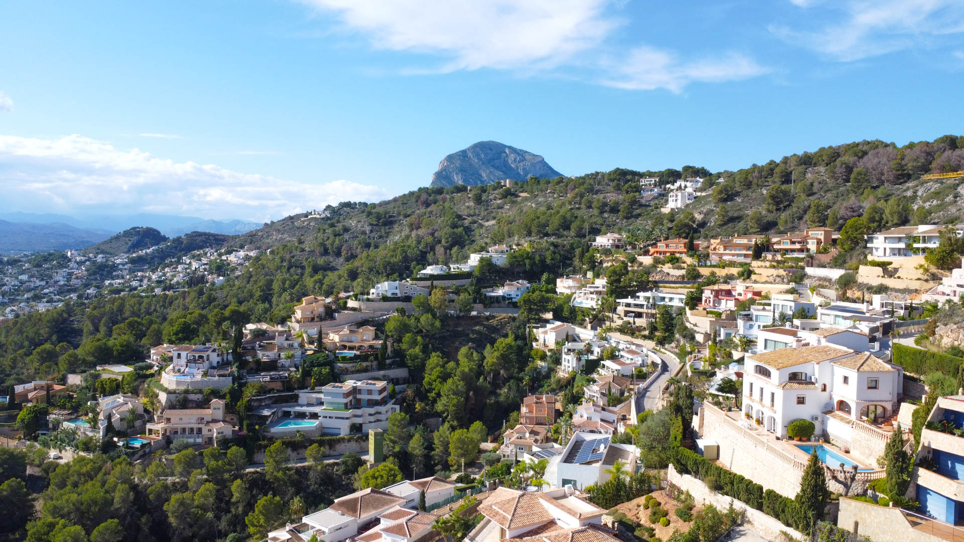 Vista aérea de la urbanización La Corona en Jávea, destacando la integración de villas mediterráneas en la ladera montañosa con el Montgó al fondo.