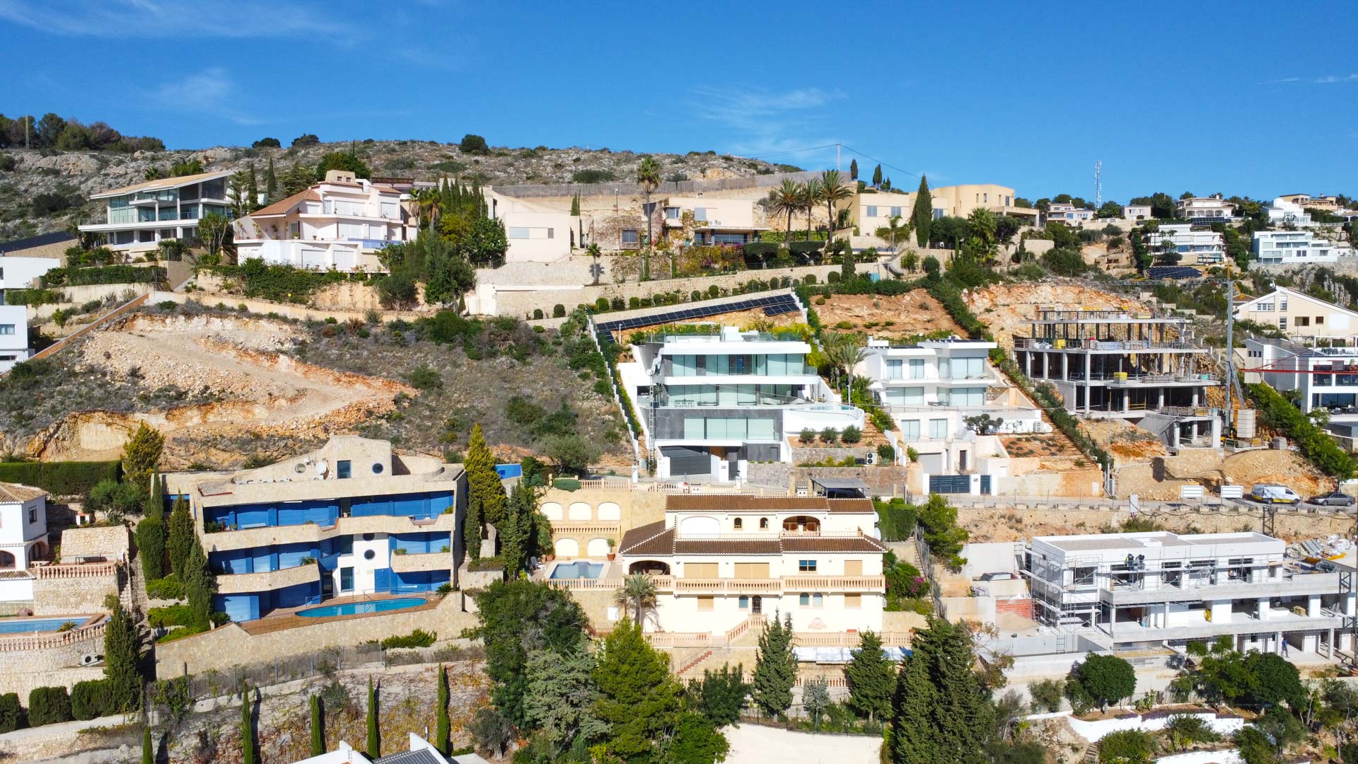 Vista aérea de la villa en la ladera de La Corona, destacando su arquitectura tradicional de tres niveles con tejados de teja y terrazas integradas en el terreno mediterráneo.