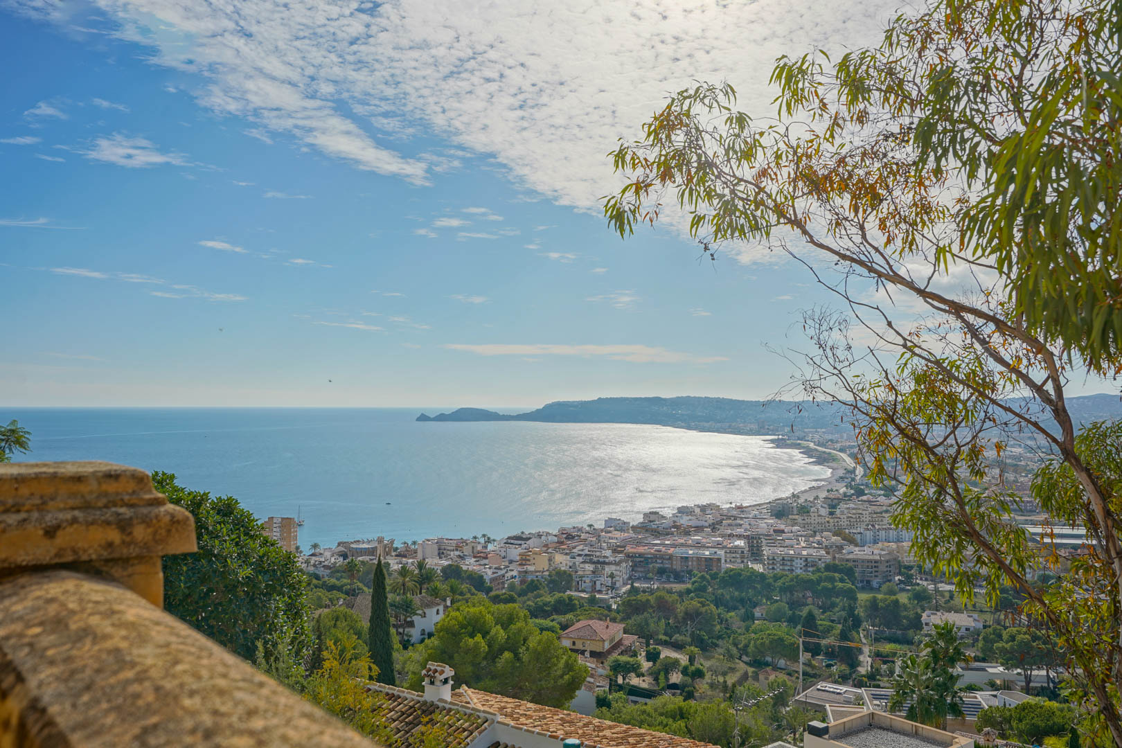 Vista panorámica desde la terraza sobre la bahía de Jávea y el Cap Negre, con el puerto y el entorno urbano en primer plano bajo un cielo despejado.