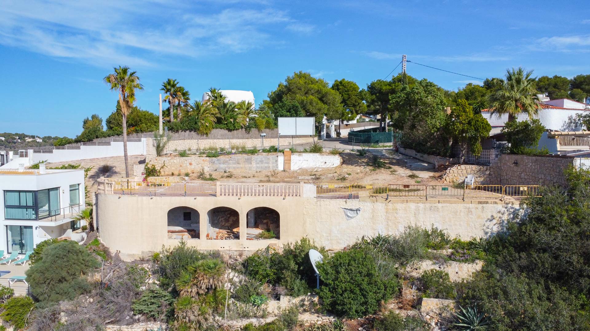Parcela elevada con estructura de arcos existente, muros de contención de piedra y vegetación mediterránea, lista para el desarrollo de una villa de lujo.