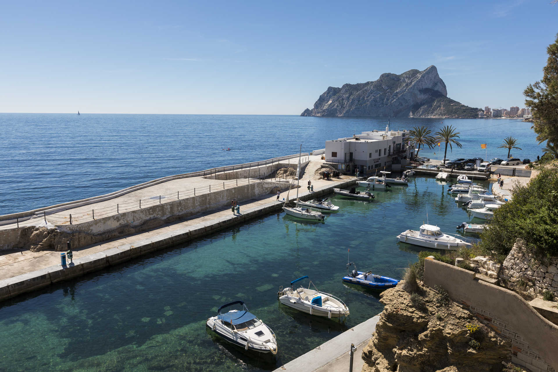 Vista panorámica del puerto deportivo cercano con el Peñón de Ifach al fondo, destacando las aguas cristalinas y la proximidad de la villa al mar Mediterráneo.