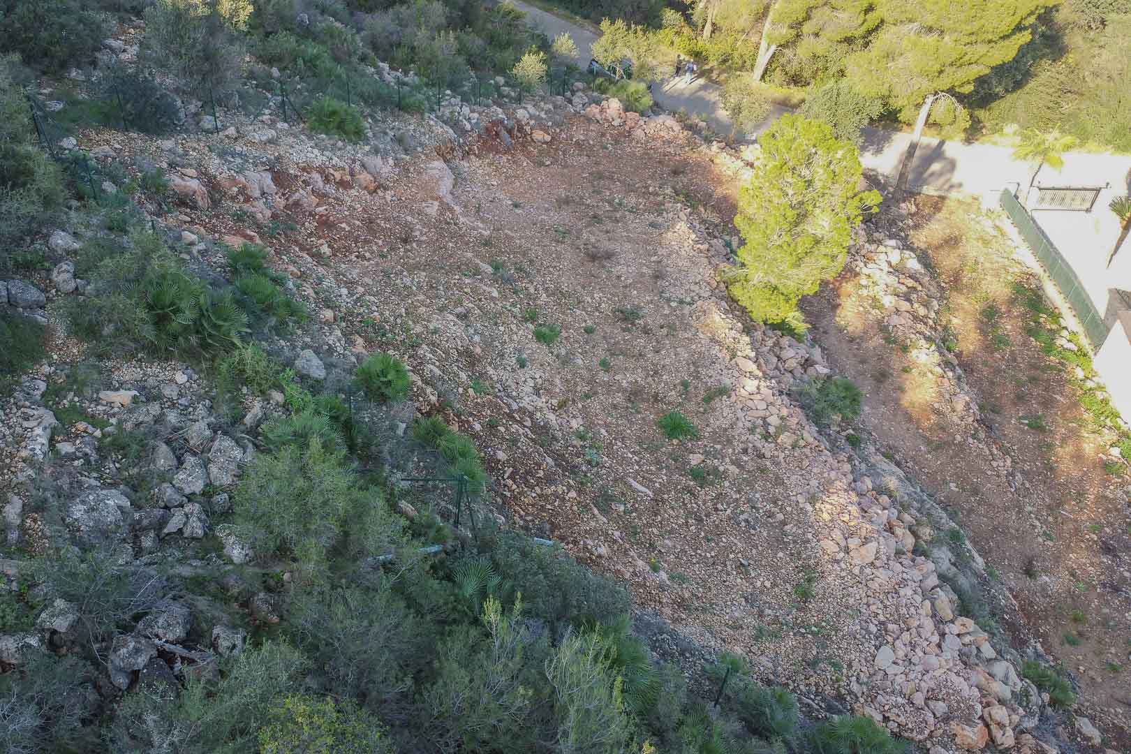 Parcela aterrazada en Montepego con suelo rocoso y despejado, rodeada de vegetación mediterránea y delimitada por un vallado perimetral junto al acceso vial.