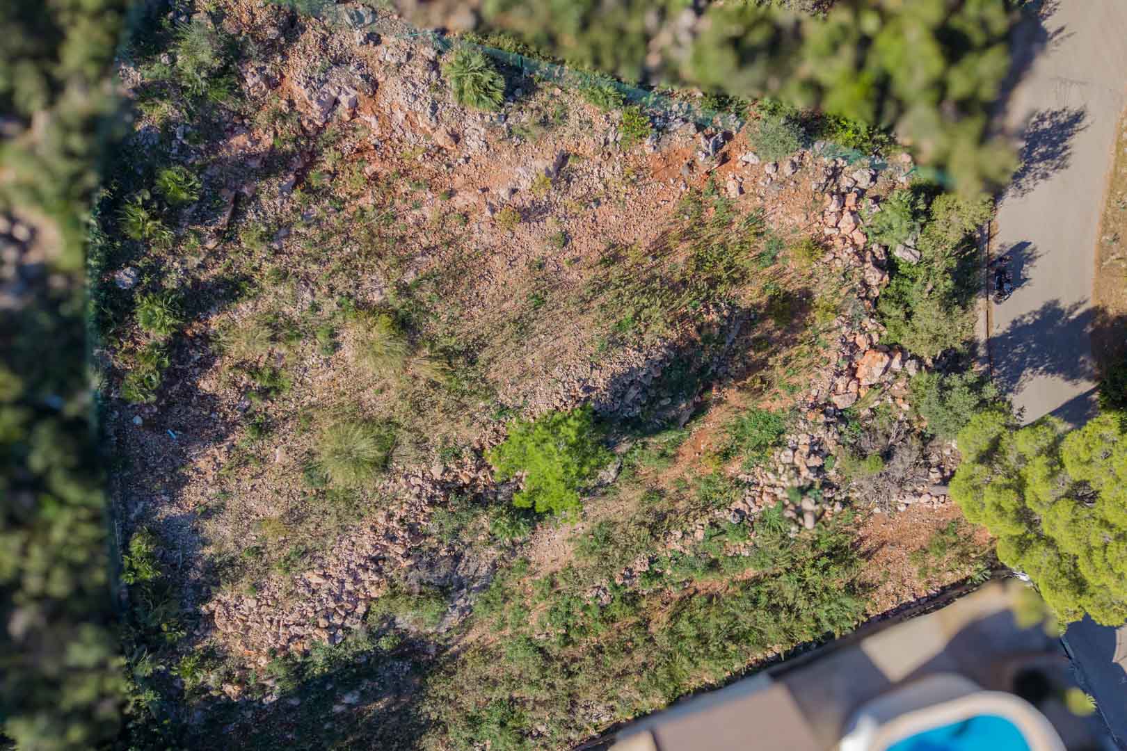 Vista aérea cenital de la parcela vallada en Montepego, mostrando el terreno rocoso natural y el acceso directo por carretera asfaltada.