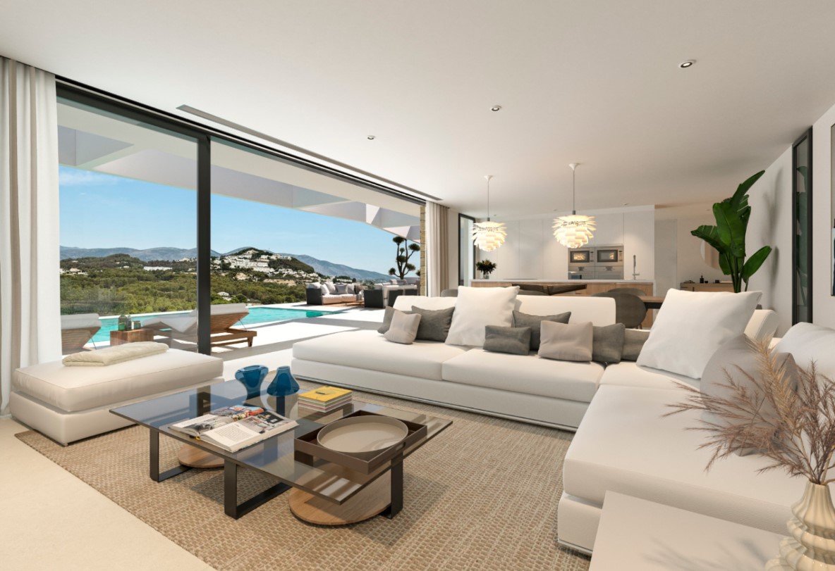 Salón de concepto abierto con sofás blancos y mesa de cristal, conectado a la terraza y piscina mediante grandes ventanales con vistas a las montañas.