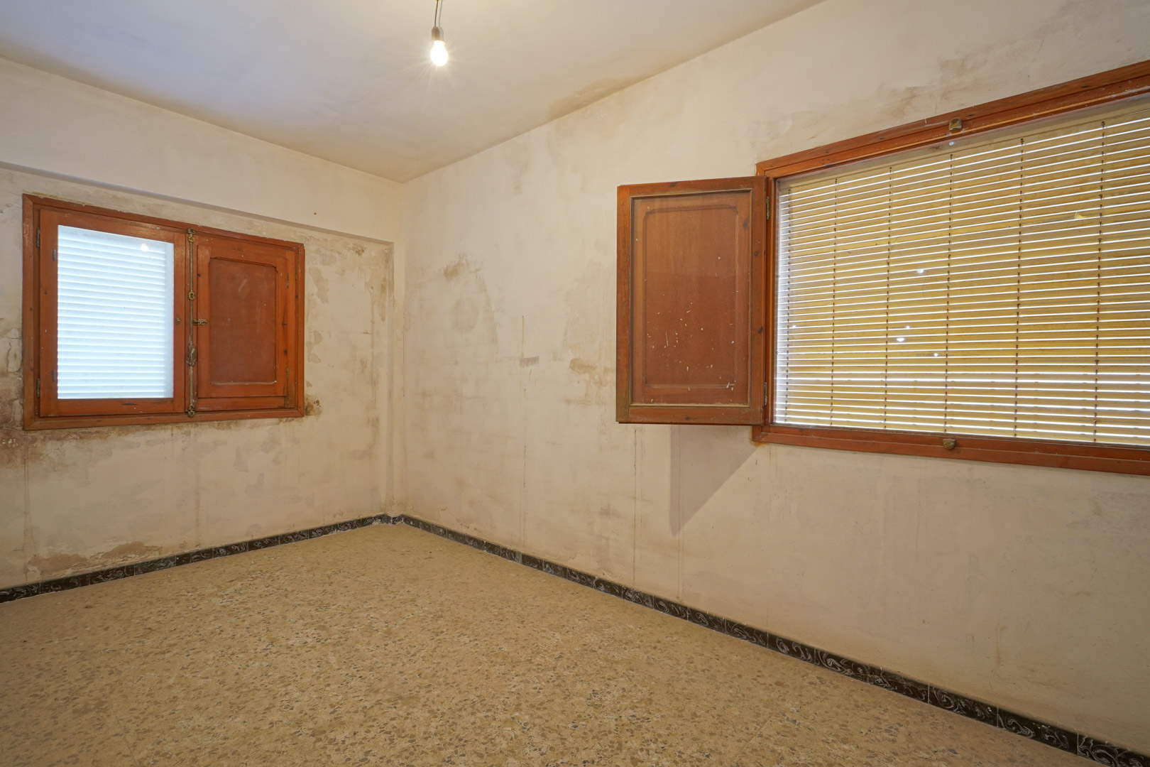 Dormitorio para reformar con suelos de terrazo original, ventanas de madera con contraventanas y paredes que ofrecen un lienzo en blanco.