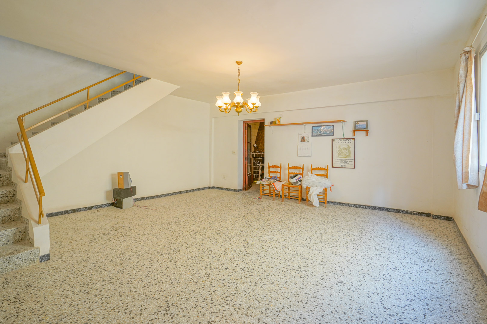 Salón principal con suelos de terrazo original, lámpara de araña clásica y escalera de acceso a la planta superior con barandilla metálica.