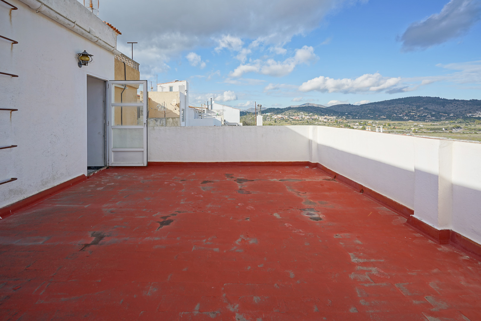 Terraza superior con suelo de baldosa roja y muros blancos, ofreciendo vistas despejadas a las montañas y al entorno rural de Benissa.