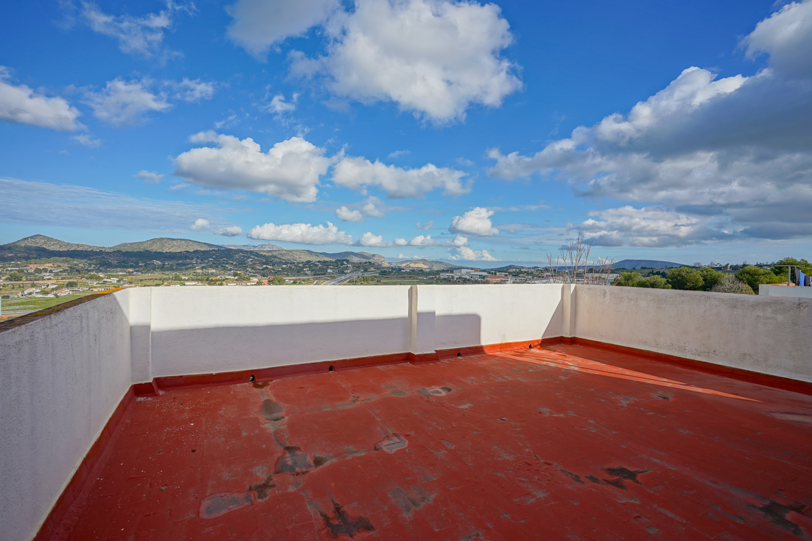 Terraza superior con suelo de color teja y muros blancos, ofreciendo vistas despejadas a las montañas y al paisaje rural de Benissa.