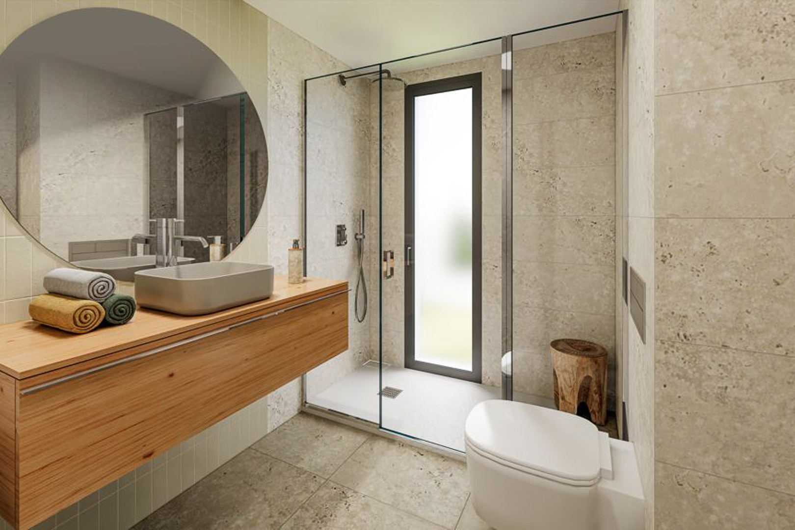 Baño moderno con mueble suspendido de madera, lavabo sobre encimera y espejo circular. Incluye ducha de obra con mampara de cristal y revestimientos en piedra natural de tono neutro.
