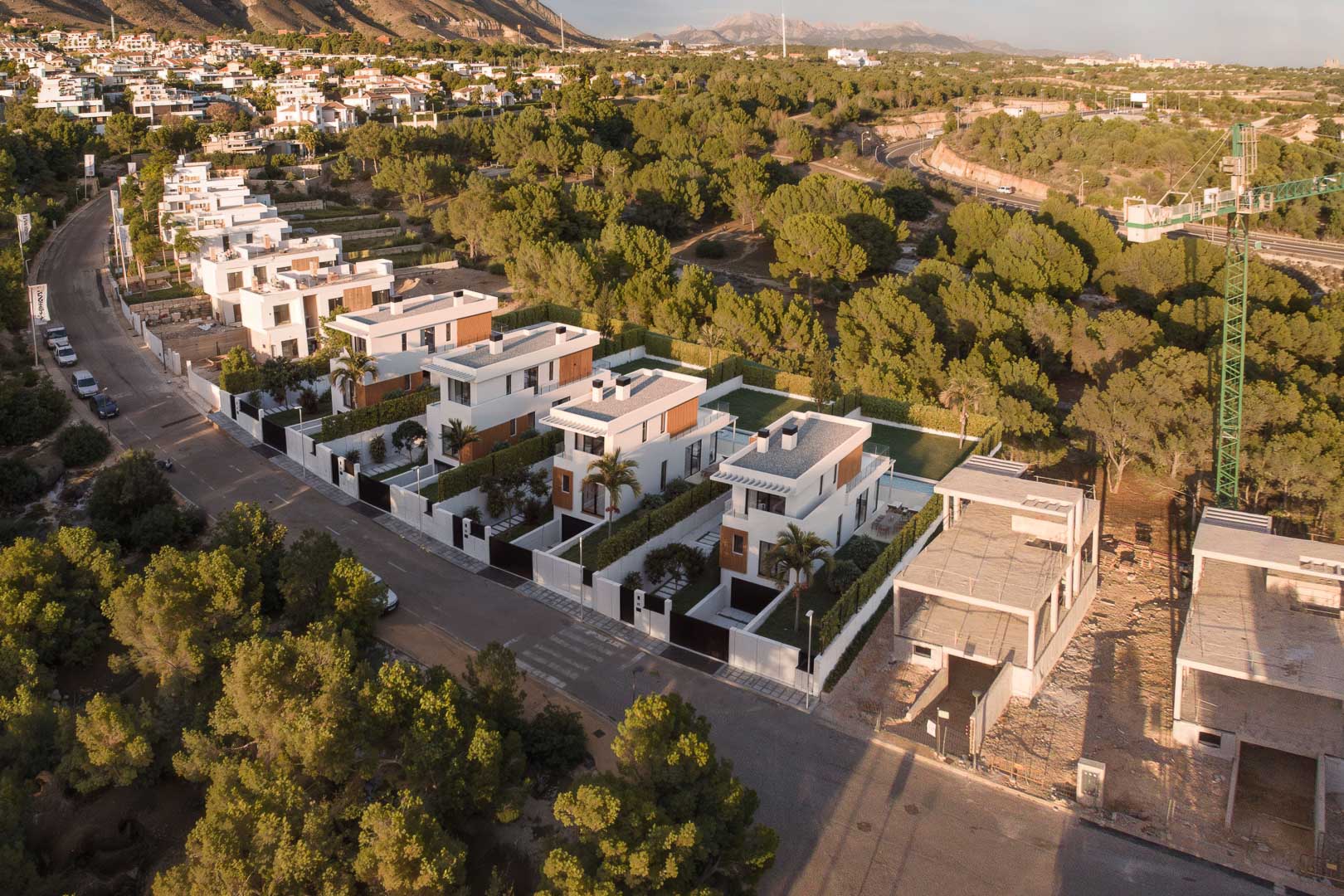 Vista aérea del complejo residencial con villas modernas de diseño cúbico, acabados en madera y piscinas privadas, integradas en un entorno natural de pinos y montañas.