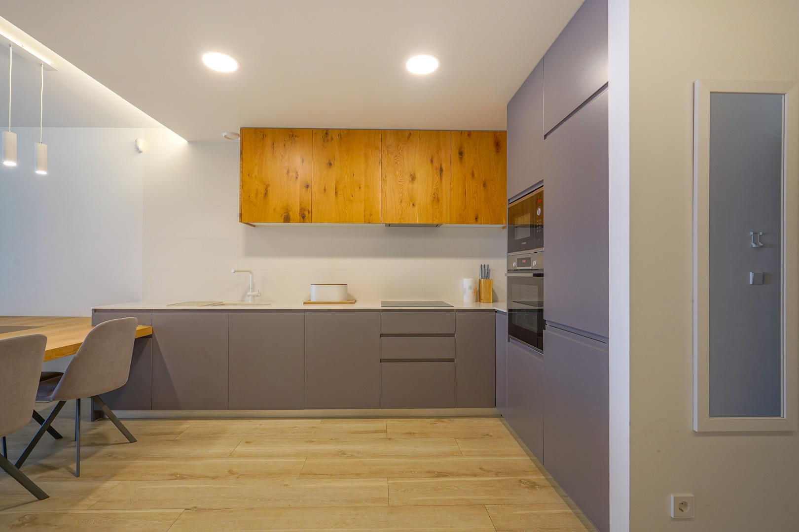 Cocina moderna de diseño minimalista con armarios en gris mate y madera natural, equipada con electrodomésticos integrados y suelos de gres con efecto madera.