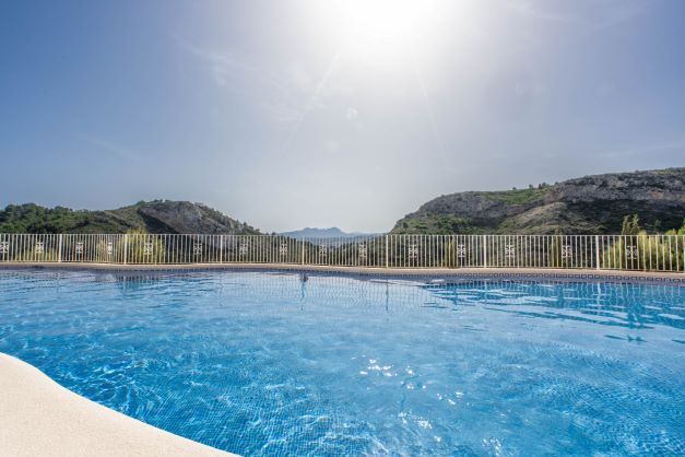 Piscina comunitaria en Monte Cala Gardens con vistas despejadas a las montañas y al parque natural bajo el sol del Mediterráneo.