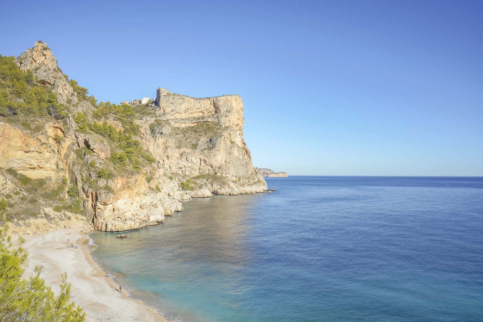 Vista panorámica de la idílica Cala Llebeig, con sus acantilados de piedra caliza y aguas cristalinas, accesible a pie desde la urbanización Monte Cala Gardens.