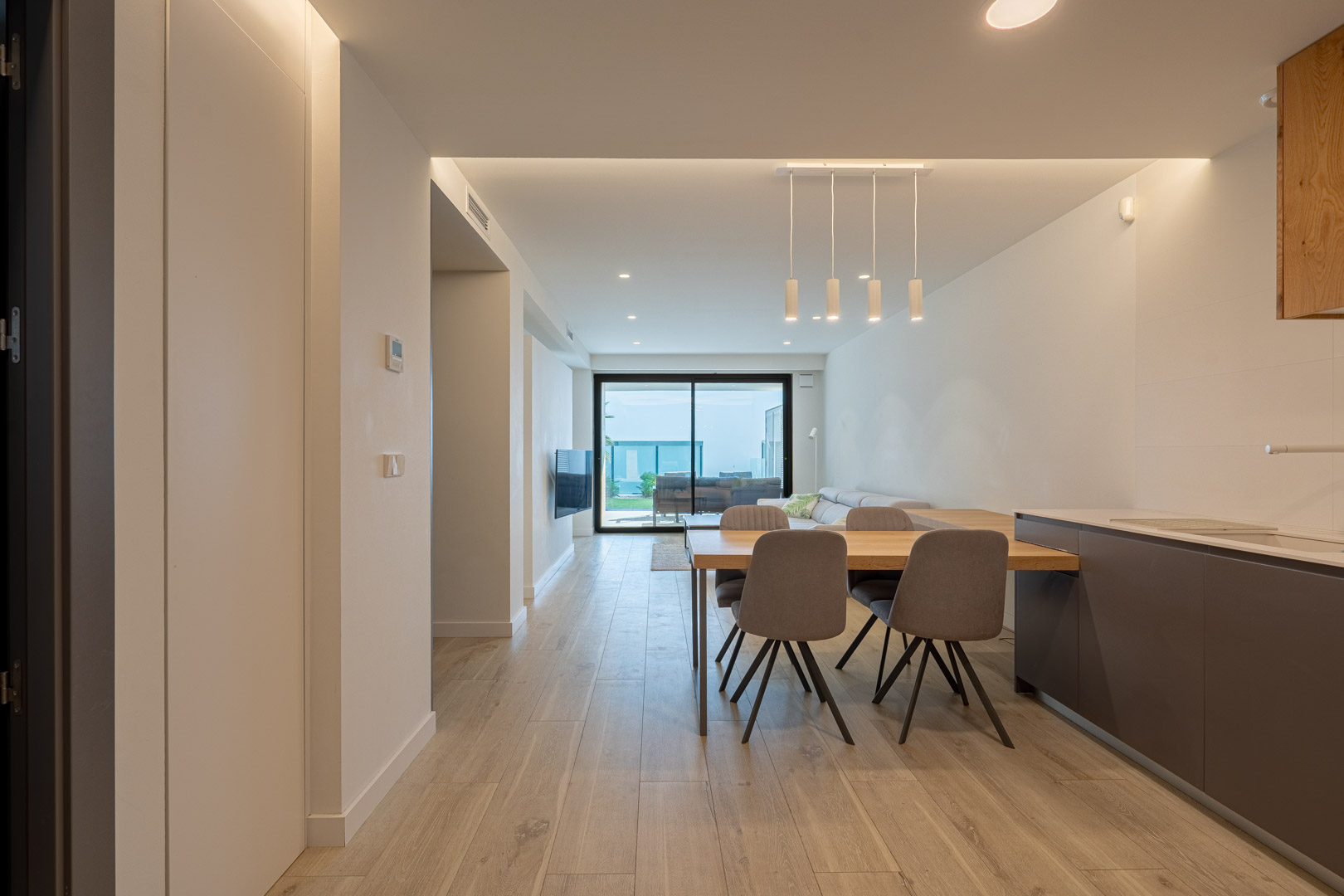 Zona de día de concepto abierto con suelos de efecto madera, iluminación LED empotrada y acceso directo a la terraza a través de amplios ventanales.