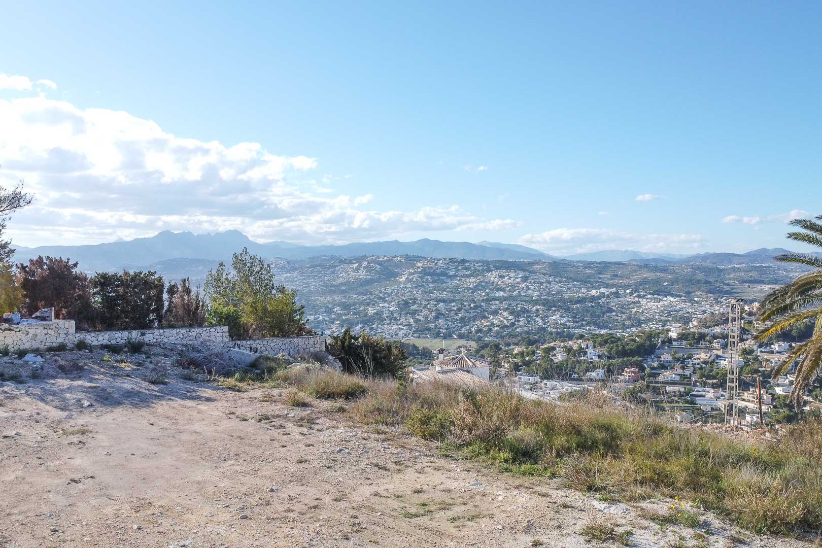 Vista panorámica de Moraira desde terreno elevado con muro de piedra y vegetación.